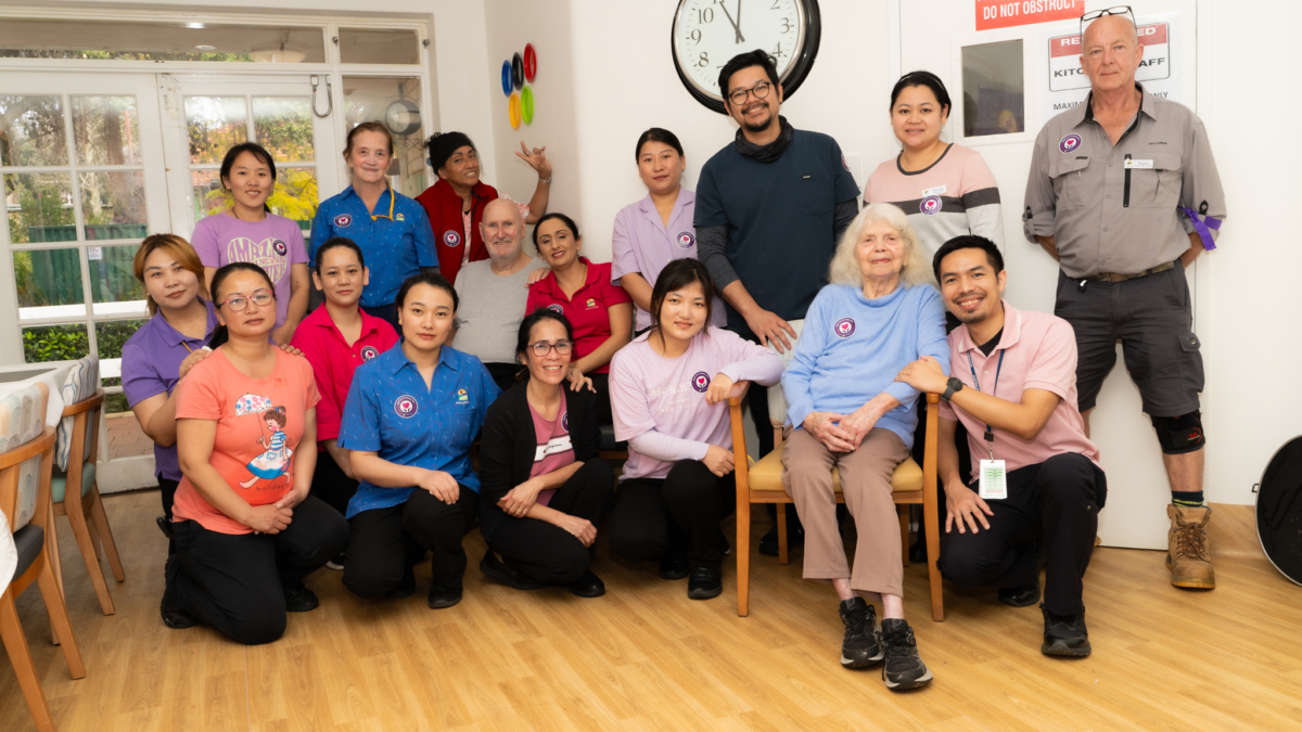 Group of staff and residents posing together, smiling and celebrating Aged Care Employee Day at Hall & Prior Kensington Park.